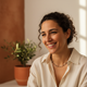 Portrait of a smiling Spanish woman in her late 20s, with a warm, happy expression, against a soft-focus background.