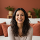 Portrait of a smiling Spanish woman with dark hair, wearing a white top, in a living room with terracotta and white decor.